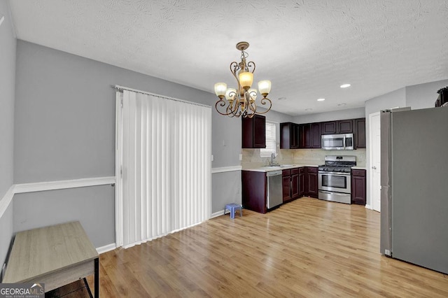 kitchen featuring light countertops, a sink, light wood-style flooring, a notable chandelier, and appliances with stainless steel finishes