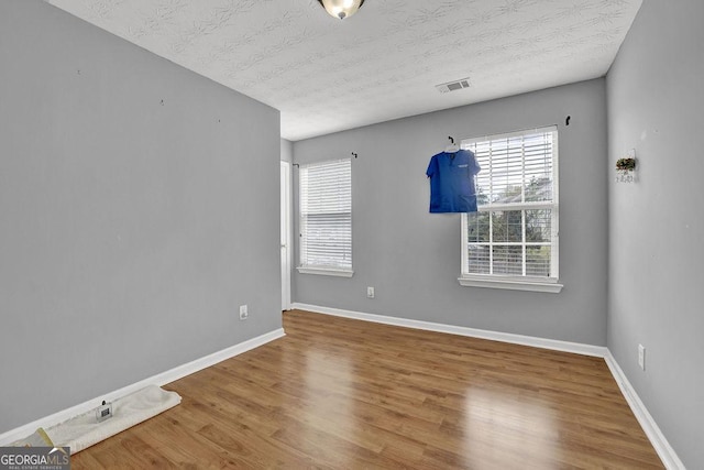 spare room with visible vents, a textured ceiling, baseboards, and wood finished floors