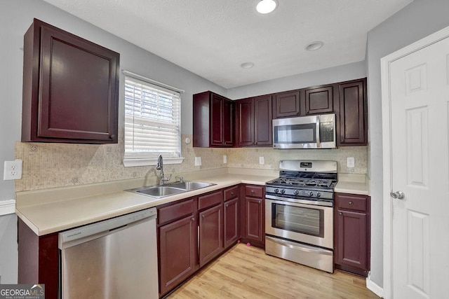 kitchen featuring light countertops, stainless steel appliances, tasteful backsplash, a sink, and light wood-style floors