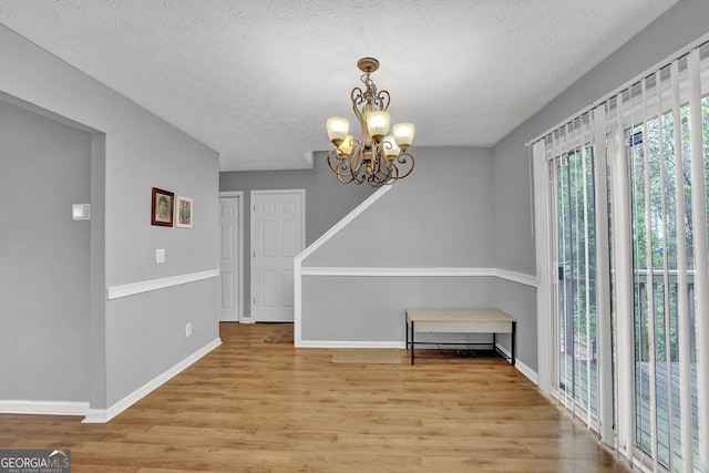 unfurnished dining area featuring a textured ceiling, wood finished floors, baseboards, and a chandelier