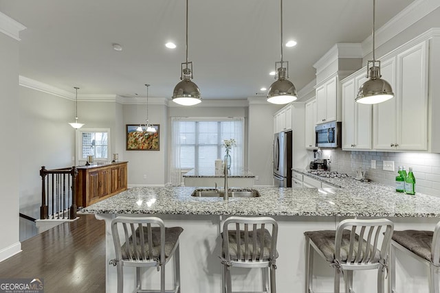 kitchen featuring appliances with stainless steel finishes, a sink, light stone countertops, white cabinetry, and ornamental molding