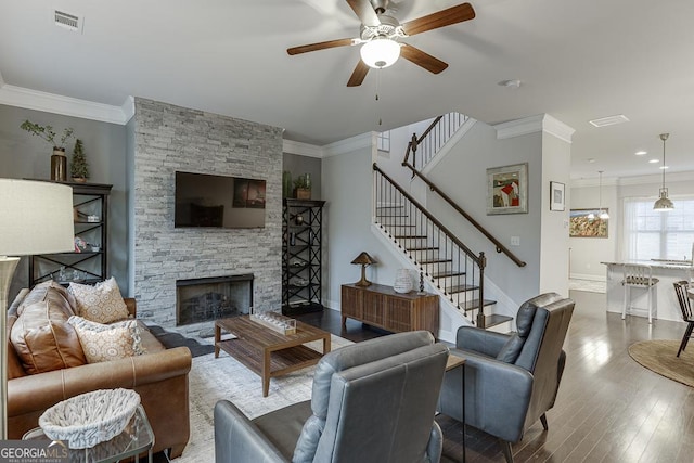 living room with crown molding, ceiling fan, stairway, wood finished floors, and a stone fireplace