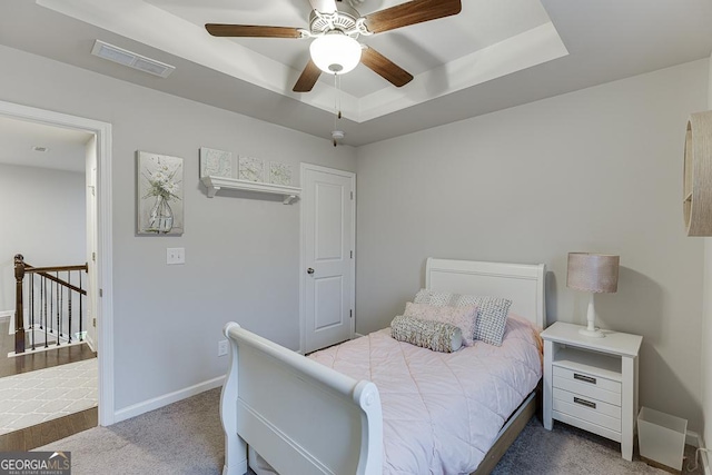 carpeted bedroom featuring a tray ceiling, baseboards, and ceiling fan