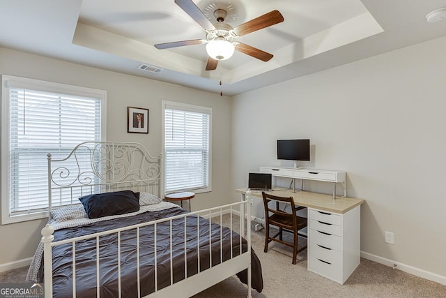 bedroom featuring a raised ceiling, multiple windows, an office area, and baseboards