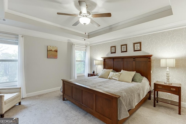 bedroom featuring light colored carpet, a tray ceiling, baseboards, ornamental molding, and ceiling fan
