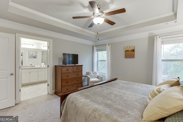 bedroom featuring a raised ceiling, light colored carpet, ornamental molding, ceiling fan, and ensuite bath