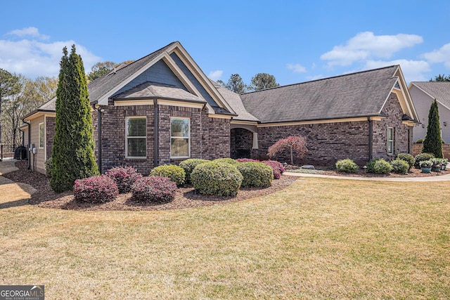 view of front of house with roof with shingles, brick siding, and a front lawn