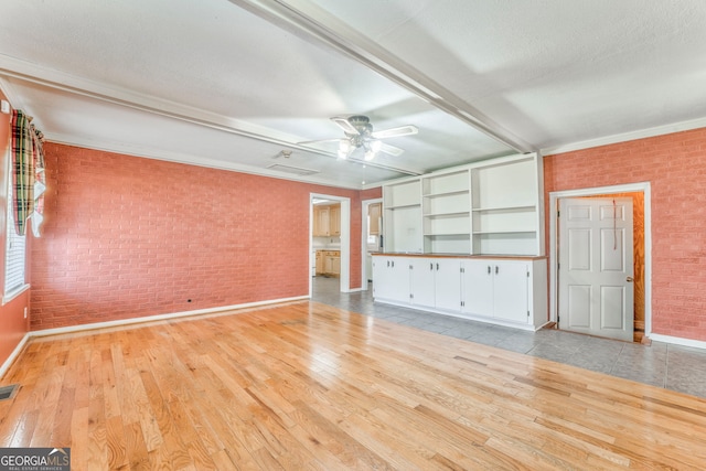 unfurnished room with visible vents, light wood-style floors, a ceiling fan, and brick wall