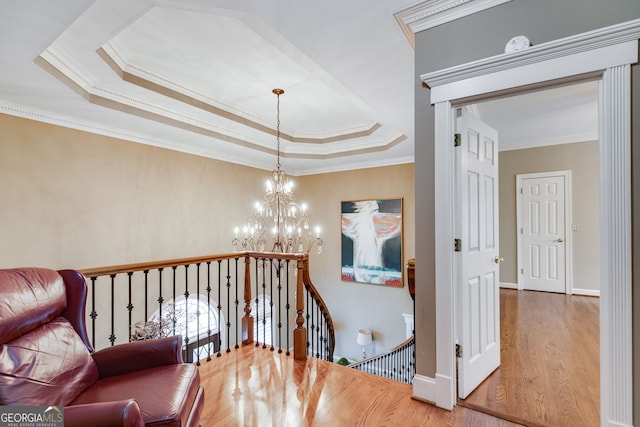 hallway featuring a raised ceiling, a notable chandelier, an upstairs landing, crown molding, and wood finished floors