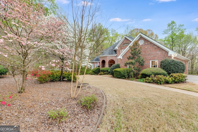view of front facade with a front yard, brick siding, and driveway