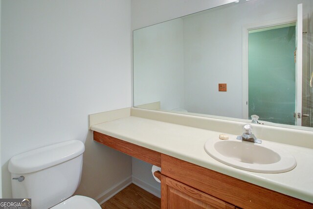 half bath featuring toilet, vanity, wood finished floors, and baseboards