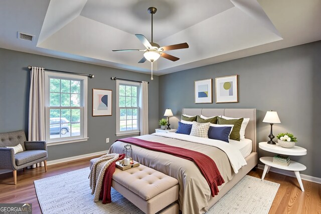 bedroom featuring a tray ceiling, wood finished floors, visible vents, and baseboards