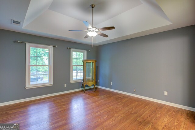empty room with light wood-style flooring, a tray ceiling, visible vents, baseboards, and a ceiling fan