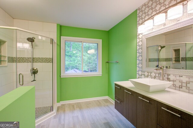 bathroom featuring wood finished floors, a stall shower, vanity, backsplash, and baseboards
