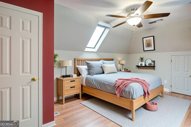 bedroom featuring baseboards, light wood-style flooring, visible vents, and lofted ceiling with skylight