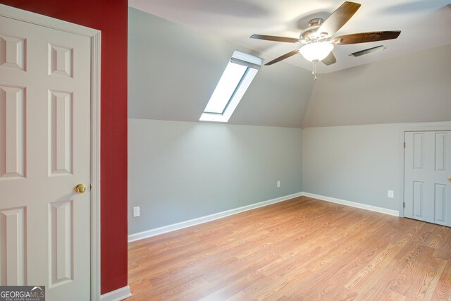 additional living space with light wood finished floors, lofted ceiling with skylight, a ceiling fan, and baseboards
