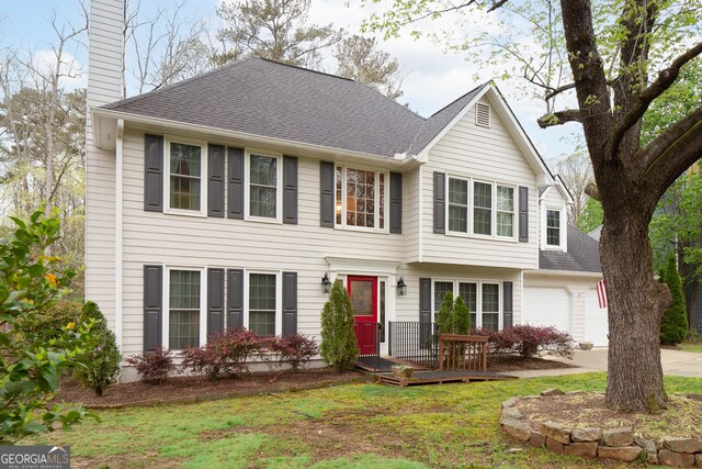 colonial inspired home featuring roof with shingles, a chimney, concrete driveway, a garage, and a front yard