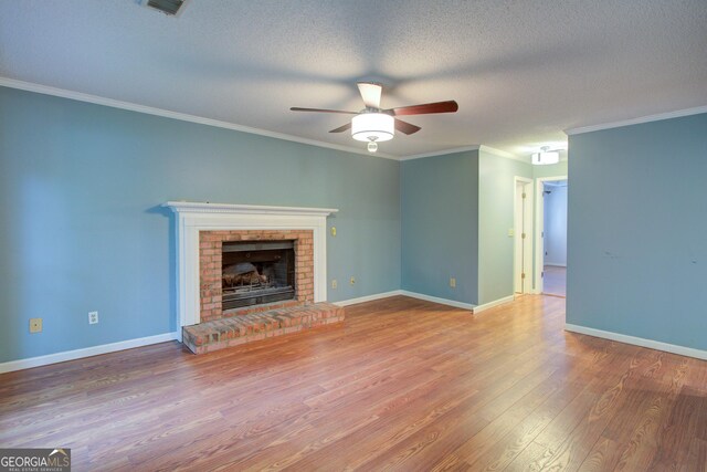 unfurnished living room featuring a brick fireplace, wood finished floors, a ceiling fan, ornamental molding, and a textured ceiling