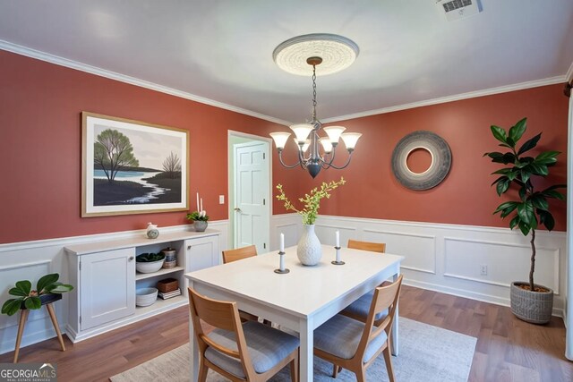dining space with a wainscoted wall, dark wood finished floors, visible vents, a chandelier, and crown molding