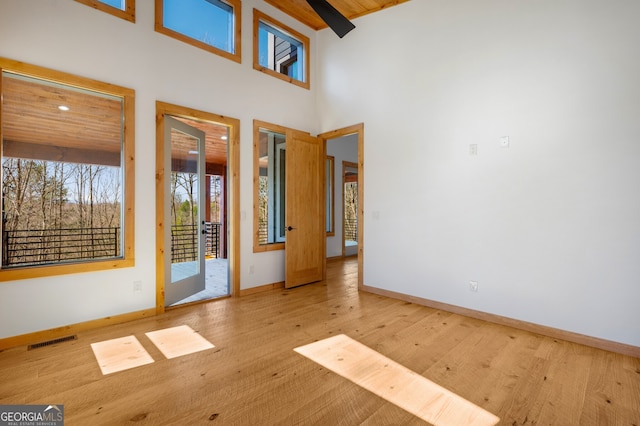 unfurnished room with baseboards, wood finished floors, visible vents, and a high ceiling