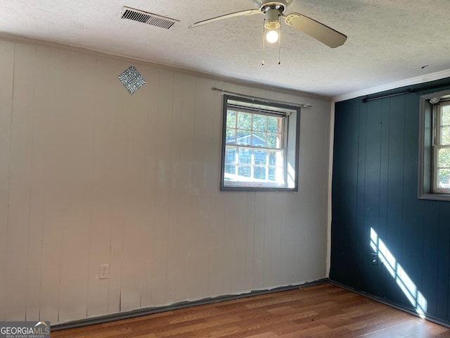empty room with wood finished floors, a textured ceiling, visible vents, ceiling fan, and ornamental molding