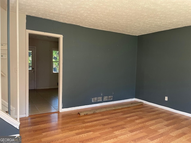 empty room with a textured ceiling, baseboards, and wood finished floors