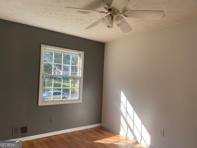 unfurnished room with a textured ceiling, visible vents, baseboards, ceiling fan, and wood finished floors