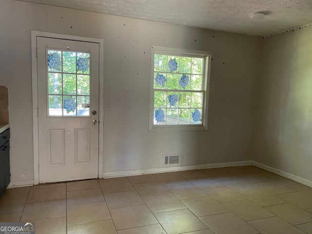 doorway featuring visible vents, baseboards, light tile patterned flooring, and a textured ceiling
