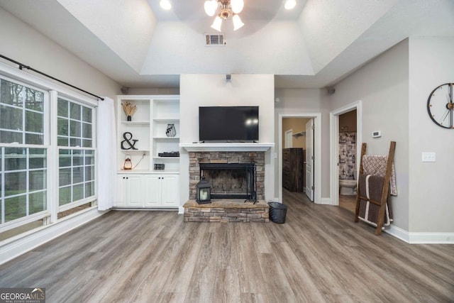 living room with a raised ceiling, ceiling fan, a fireplace, and light wood-style flooring
