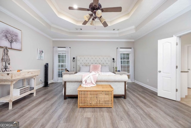 bedroom with light wood-style flooring, baseboards, and a raised ceiling