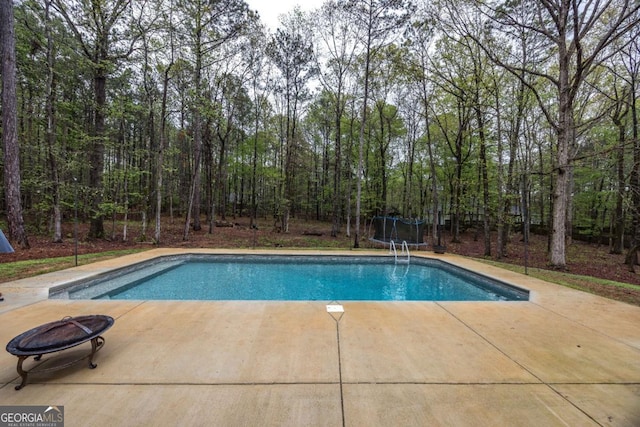 outdoor pool with a trampoline, a patio area, and a fire pit