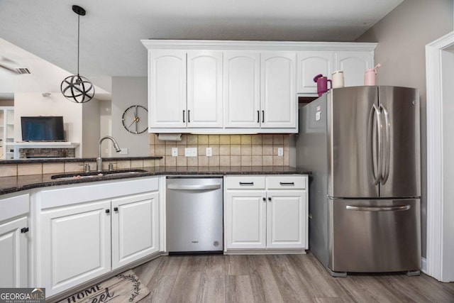 kitchen featuring dark stone countertops, a sink, light wood-style floors, white cabinetry, and stainless steel appliances
