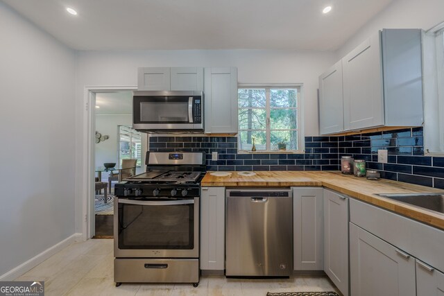 kitchen with butcher block countertops, decorative backsplash, and stainless steel appliances
