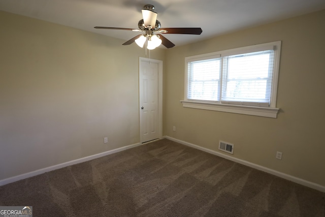 unfurnished room featuring baseboards, visible vents, dark colored carpet, and ceiling fan