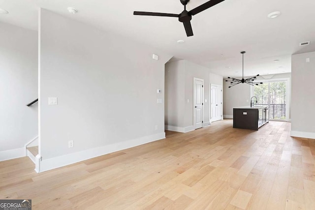 unfurnished living room featuring ceiling fan, light wood-type flooring, baseboards, and a chandelier