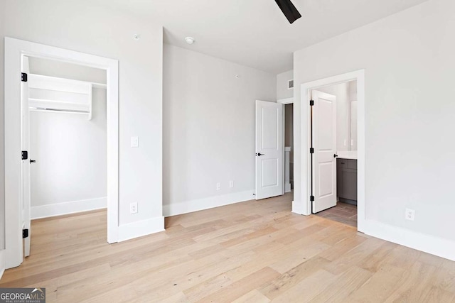 unfurnished bedroom featuring light wood finished floors, baseboards, a spacious closet, ensuite bathroom, and a closet