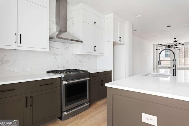 kitchen with gas stove, wall chimney range hood, a sink, white cabinets, and light countertops