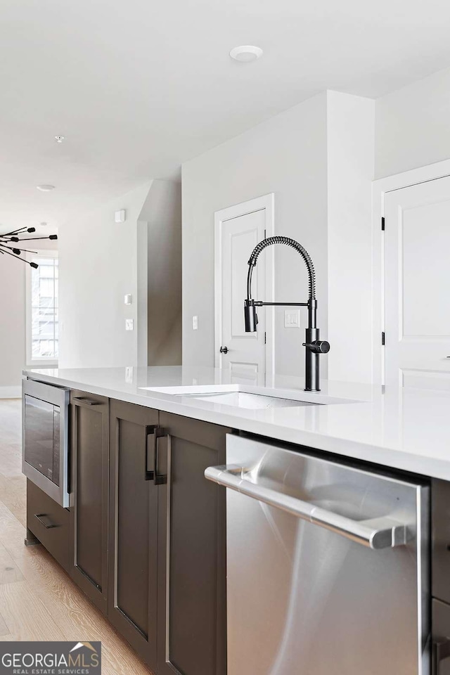 kitchen with stainless steel appliances, light countertops, a sink, and light wood-type flooring