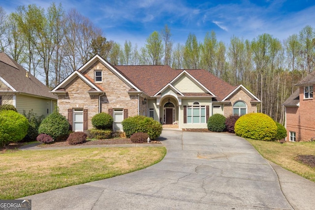 view of front of home with brick siding, a front yard, concrete driveway, and roof with shingles