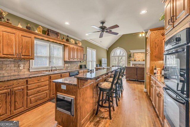 kitchen with a kitchen bar, a kitchen island, a sink, ceiling fan, and dobule oven black