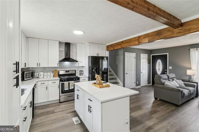 kitchen featuring wall chimney exhaust hood, wood finished floors, appliances with stainless steel finishes, open floor plan, and beamed ceiling