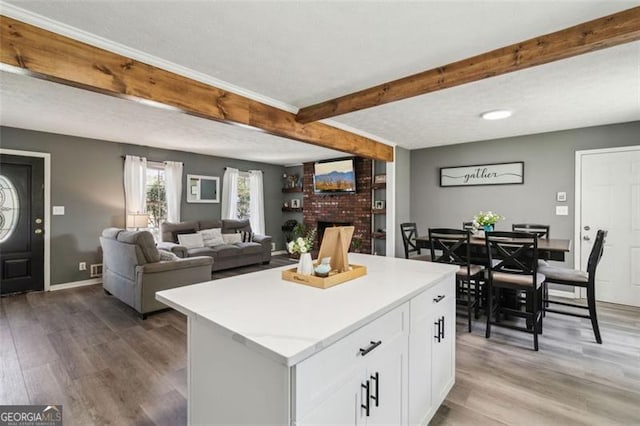 kitchen featuring beam ceiling, a fireplace, a center island, white cabinets, and light wood-style floors