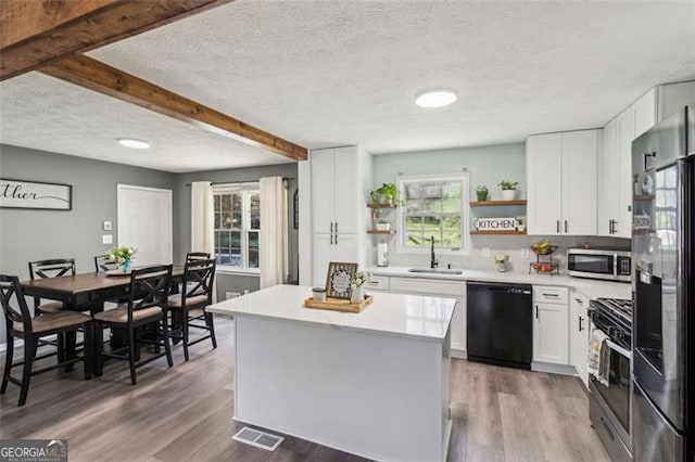 kitchen featuring light countertops, open shelves, a sink, appliances with stainless steel finishes, and wood finished floors