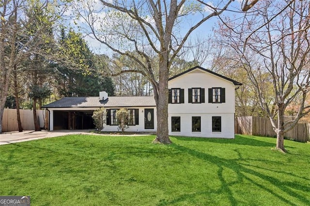 rear view of property featuring an attached carport, concrete driveway, fence, and a lawn