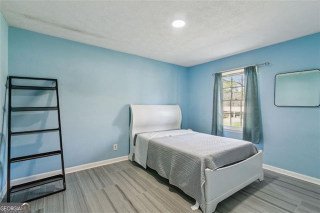 bedroom with baseboards, wood finished floors, and a textured ceiling