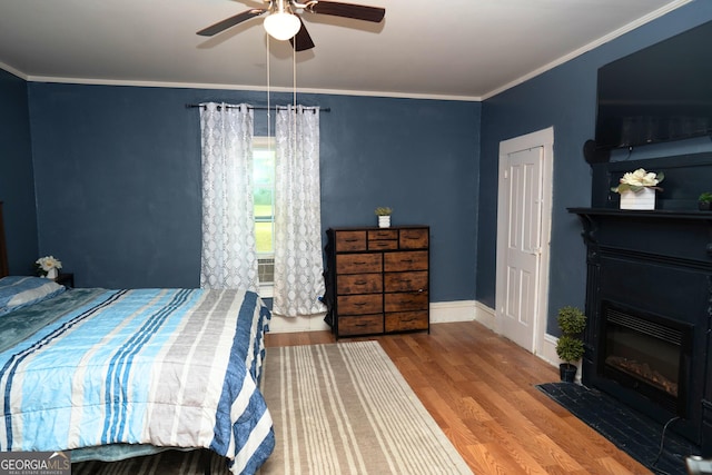 bedroom featuring crown molding, baseboards, ceiling fan, a glass covered fireplace, and wood finished floors