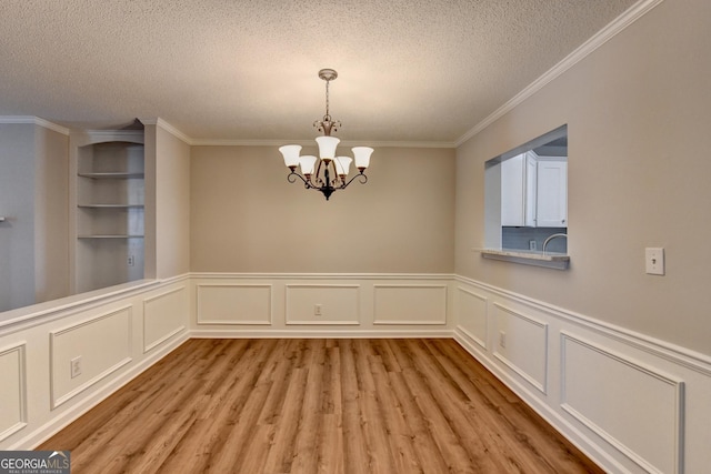 unfurnished dining area featuring light wood finished floors, a notable chandelier, ornamental molding, and a textured ceiling