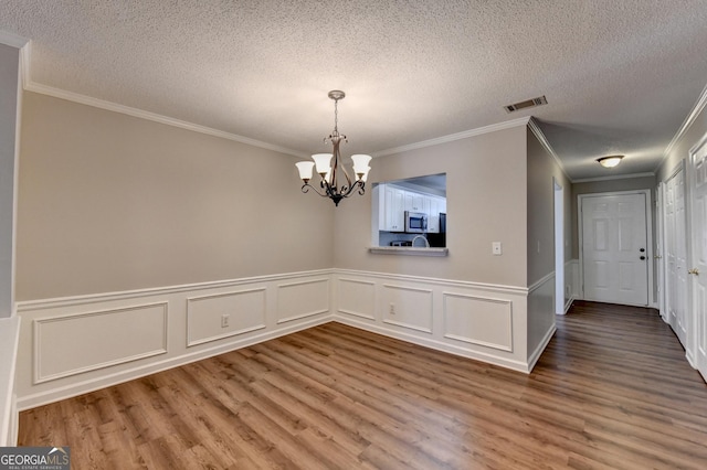 unfurnished dining area featuring a textured ceiling, visible vents, a notable chandelier, and wood finished floors