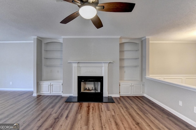 unfurnished living room featuring crown molding, a ceiling fan, wood finished floors, and built in shelves