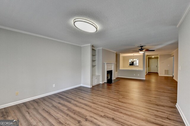 unfurnished living room with a textured ceiling, visible vents, crown molding, a fireplace, and wood finished floors